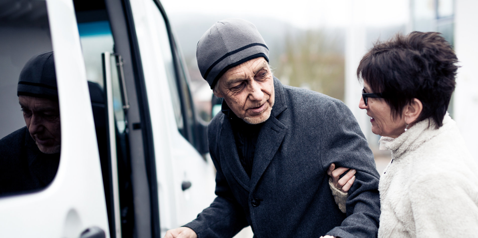 elderly woman helping a senior man in boarding a van