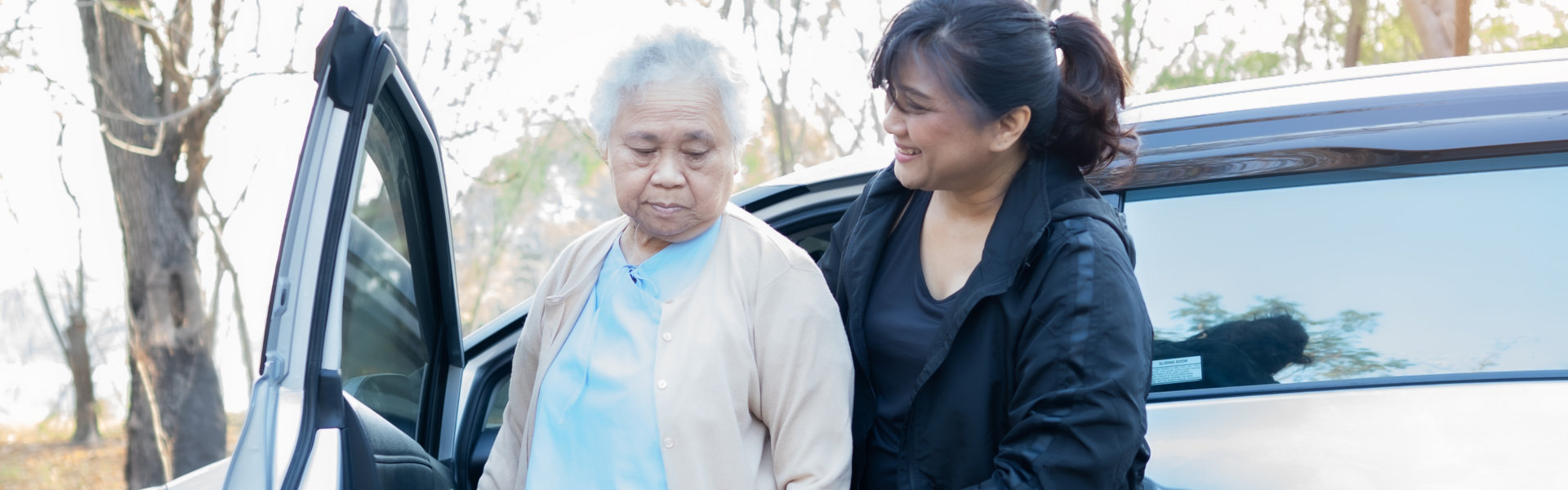 woman guiding senior woman in getting off the vehicle